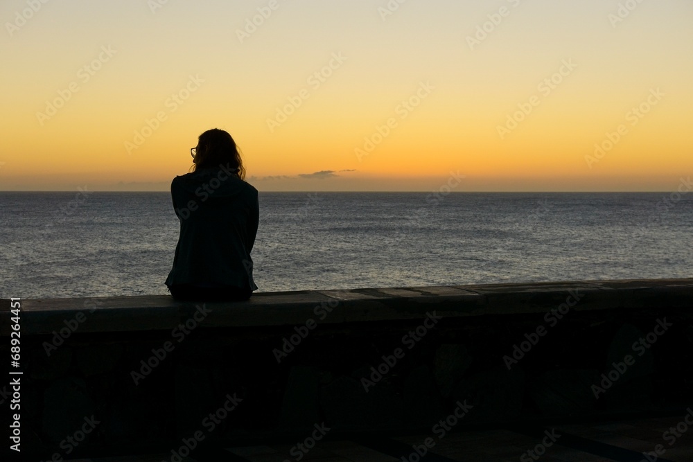 Rear view of a woman silhouette on the beach at sunset against sun in Maspalomas, Gran Canaria, Spain