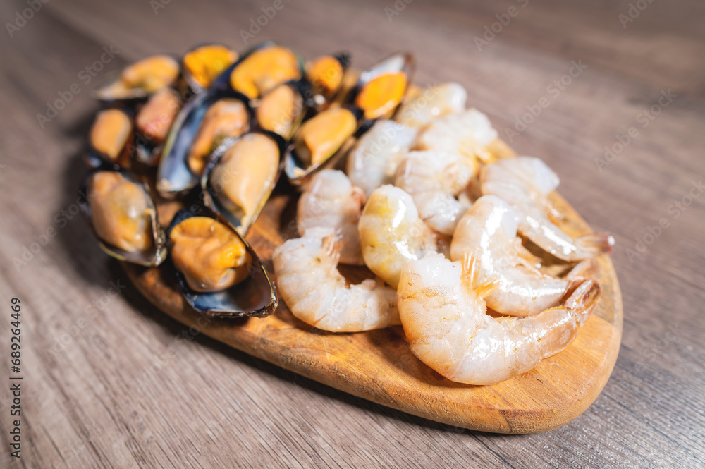 Side view of a plate of mixed seafood being served as an appetizer. Peeled shrimp and mussels in the shell lie on a wooden plate, close-up