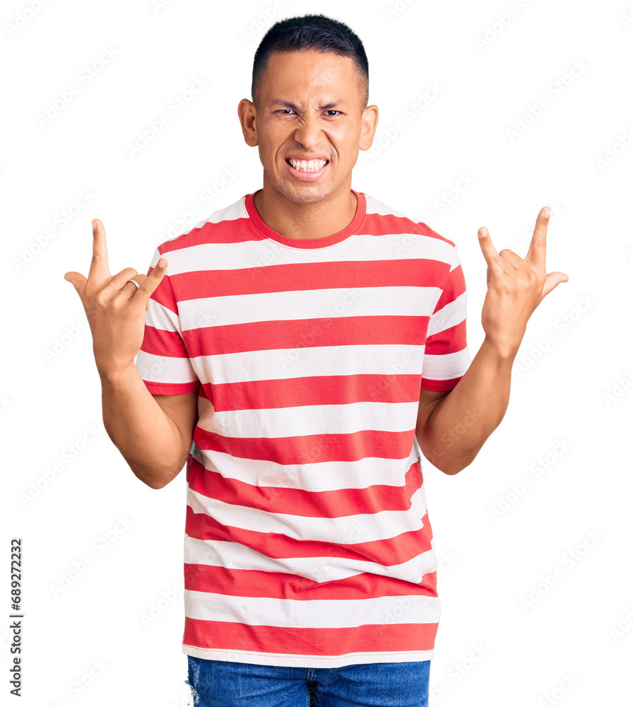 Young handsome latin man wearing casual clothes shouting with crazy expression doing rock symbol with hands up. music star. heavy concept. Young handsome latin man wearing casual clothes shouting with crazy expression doing rock symbol with hands up. music star. heavy concept.