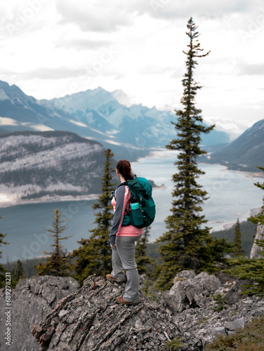 A female hiker stands on the side of a mountain looking at a view of a large reservoir below in Alberta, Canada