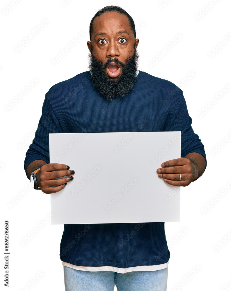 Young african american man holding blank empty banner scared and amazed with open mouth for surprise, disbelief face Young african american man holding blank empty banner scared and amazed with open mouth for surprise, disbelief face