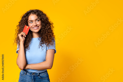 Thoughtful woman with credit card looking at free space on yellow photo