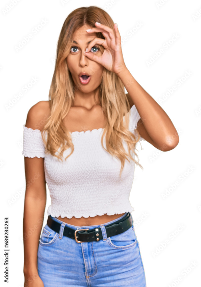 Beautiful blonde young woman wearing casual white tshirt doing ok gesture shocked with surprised face, eye looking through fingers. unbelieving expression. Beautiful blonde young woman wearing casual white tshirt doing ok gesture shocked with surprised face, eye looking through fingers. unbelieving expression.