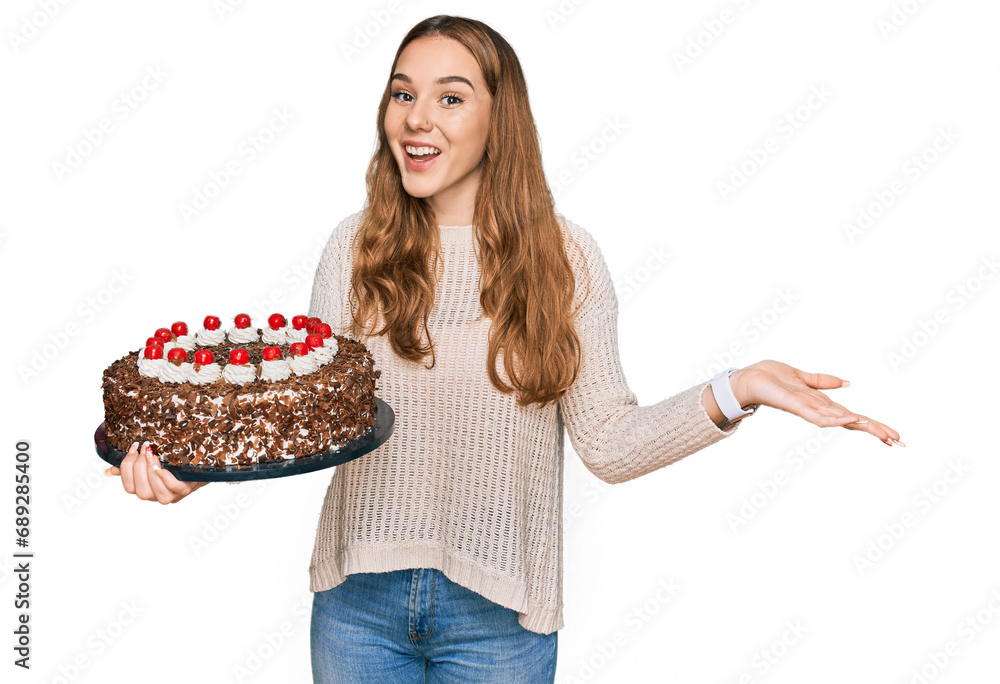 Young blonde woman celebrating birthday holding big chocolate cake celebrating victory with happy smile and winner expression with raised hands Young blonde woman celebrating birthday holding big chocolate cake celebrating victory with happy smile and winner expression with raised hands