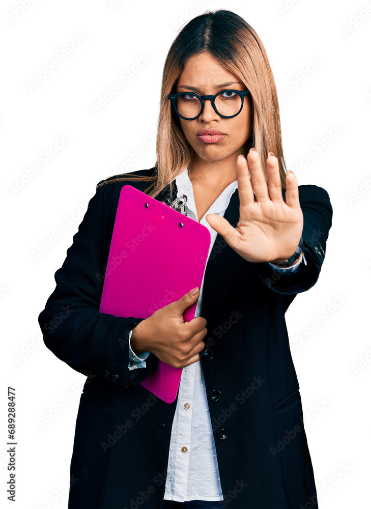 Young hispanic business woman holding clipboard with blank space doing stop sing with palm of the hand. warning expression with negative and serious gesture on the face. Young hispanic business woman holding clipboard with blank space doing stop sing with palm of the hand. warning expression with negative and serious gesture on the face.