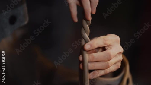 Close-up female hands making clay pigtail form detail. Woman potter wearing warm plaid shirt shapes craft clay tableware in pottery studio. Working process modeling in ceramic workshop photo