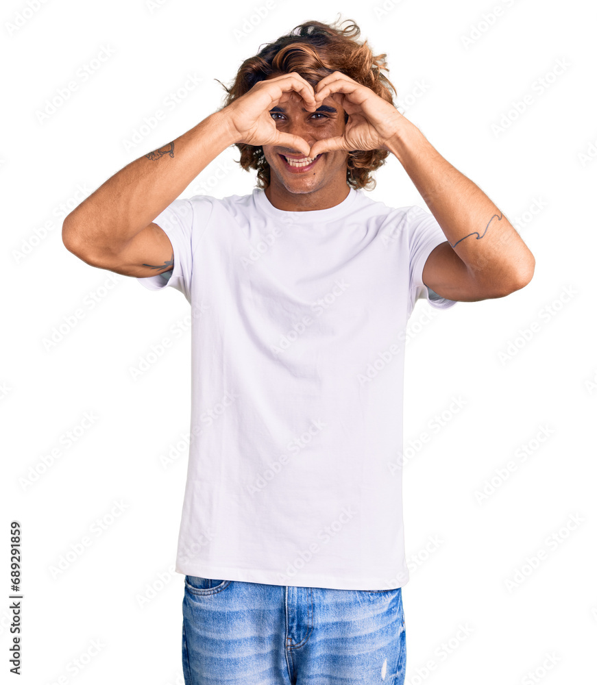 Young hispanic man wearing casual white tshirt doing heart shape with hand and fingers smiling looking through sign Young hispanic man wearing casual white tshirt doing heart shape with hand and fingers smiling looking through sign
