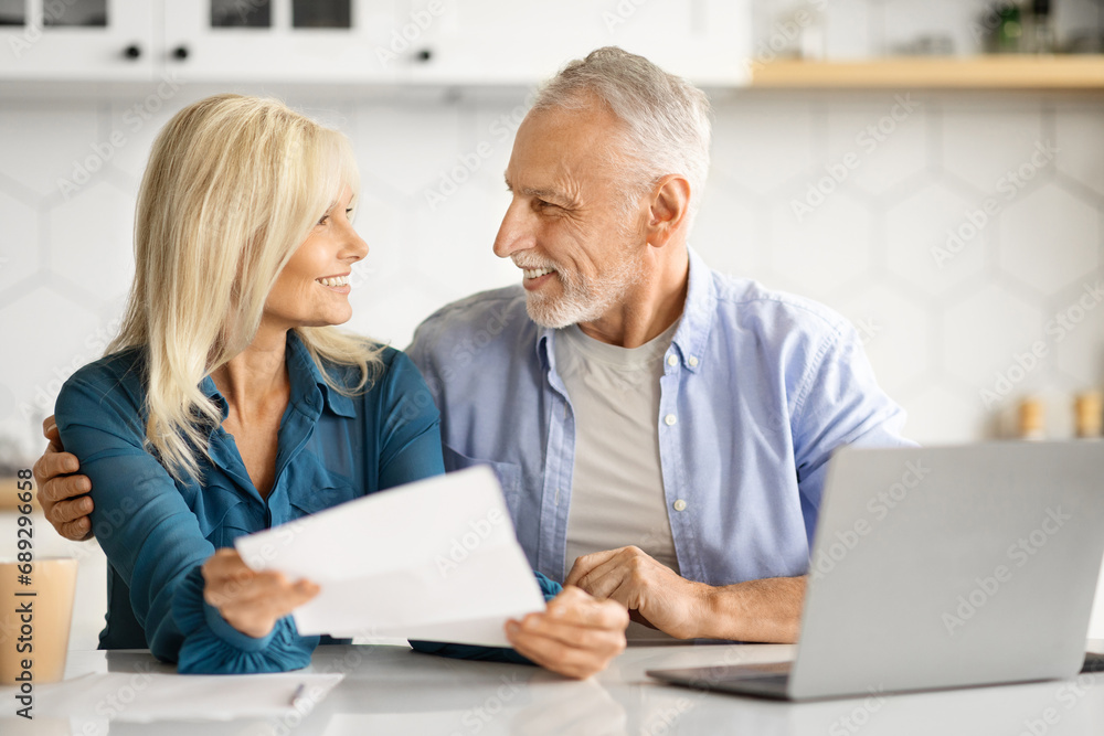 Portrait Of Cheerful Elderly Spouses Sitting In Kitchen And Checking Financial Papers Portrait Of Cheerful Elderly Spouses Sitting In Kitchen And Checking Financial Papers