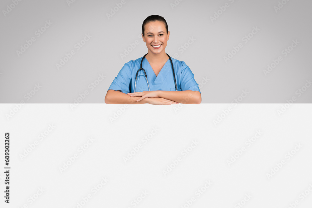 Medical ad. Cheerful european female doctor leaning on big blank advertising board with free space for your text or offer Medical ad. Cheerful european female doctor leaning on big blank advertising board with free space for your text or offer