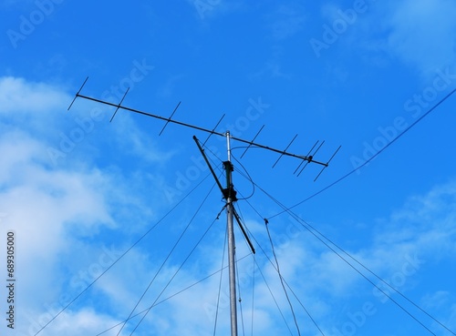 A VHF radio antenna with stay ropes against a cloudy blue sky