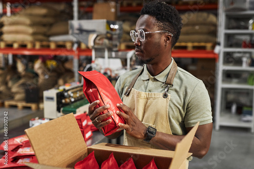 Waist up portrait of Black young man holding coffee bag doing quality control in packaging department, copy space photo