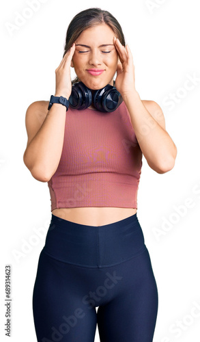 Beautiful caucasian young woman wearing gym clothes and using headphones with hand on head, headache because stress. suffering migraine.