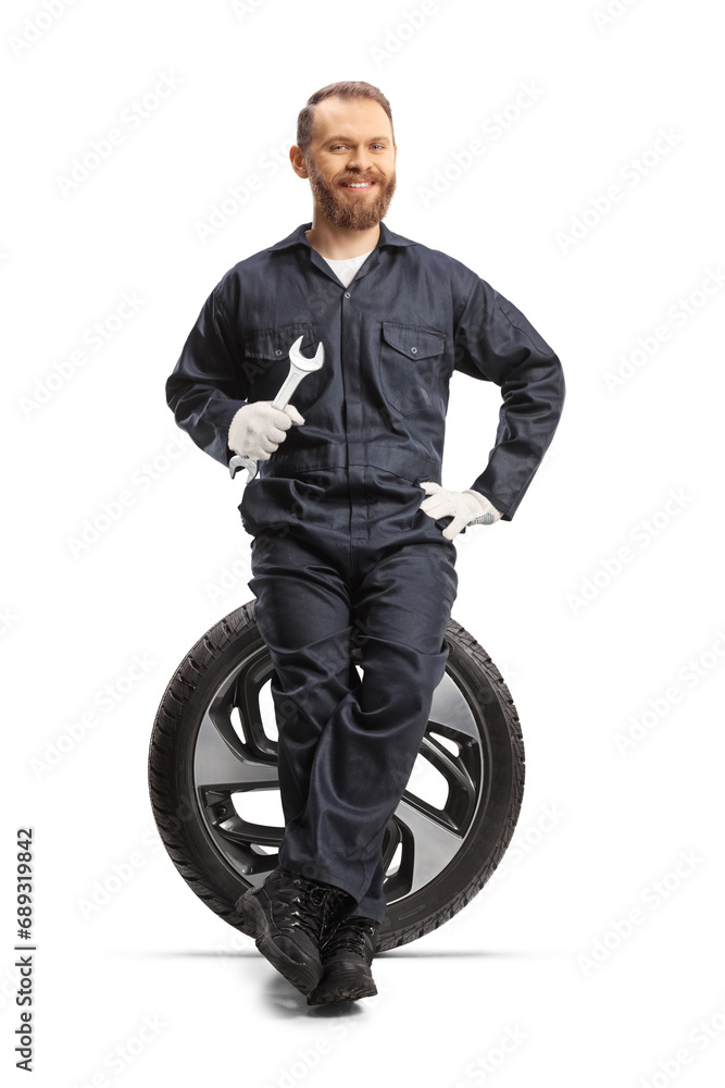 Obraz premium Car mechanic holding a wrench and sitting on a tire