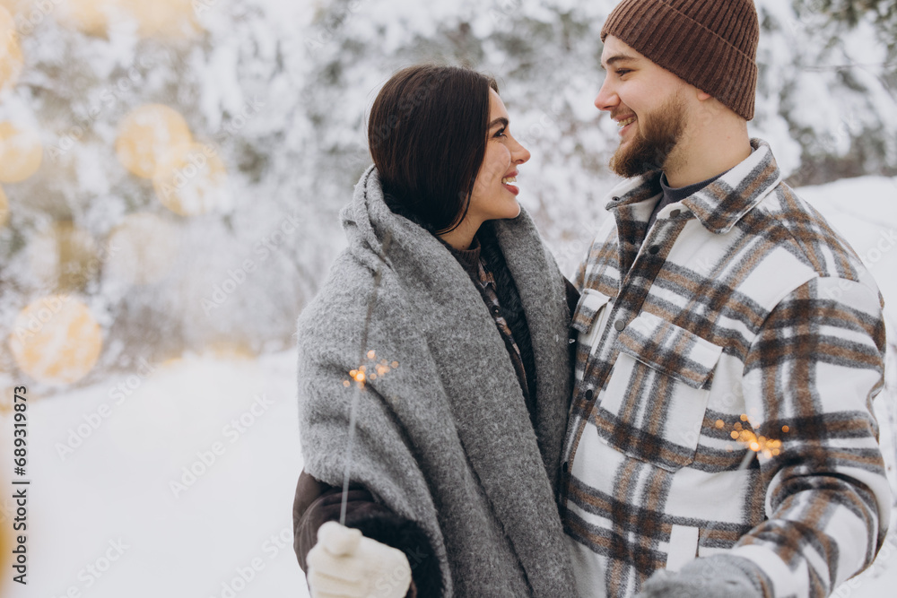 Fototapeta premium Happy romantic couple in love holding sparklers in snowy winter forest