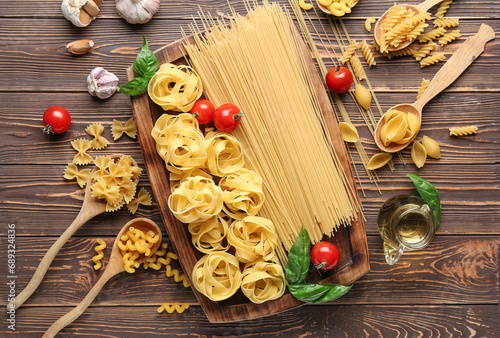 Composition with different uncooked pasta, spices and tomatoes on wooden background photo