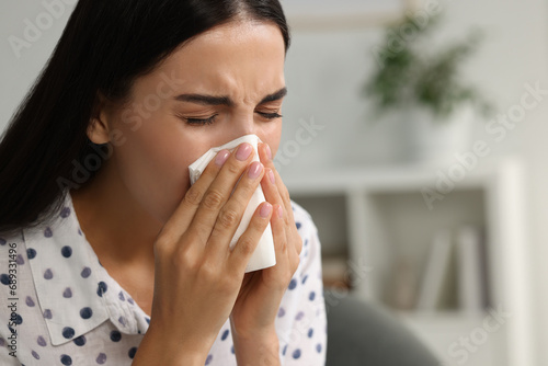 Suffering from allergy. Young woman blowing her nose in tissue indoors, closeup. Space for text