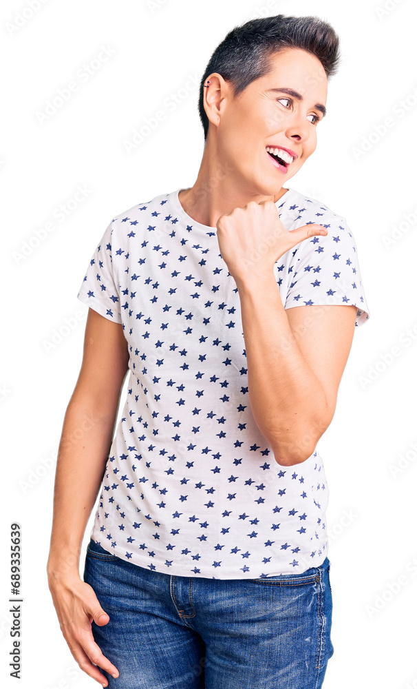 Young woman with short hair wearing casual clothes smiling with happy face looking and pointing to the side with thumb up. Young woman with short hair wearing casual clothes smiling with happy face looking and pointing to the side with thumb up.