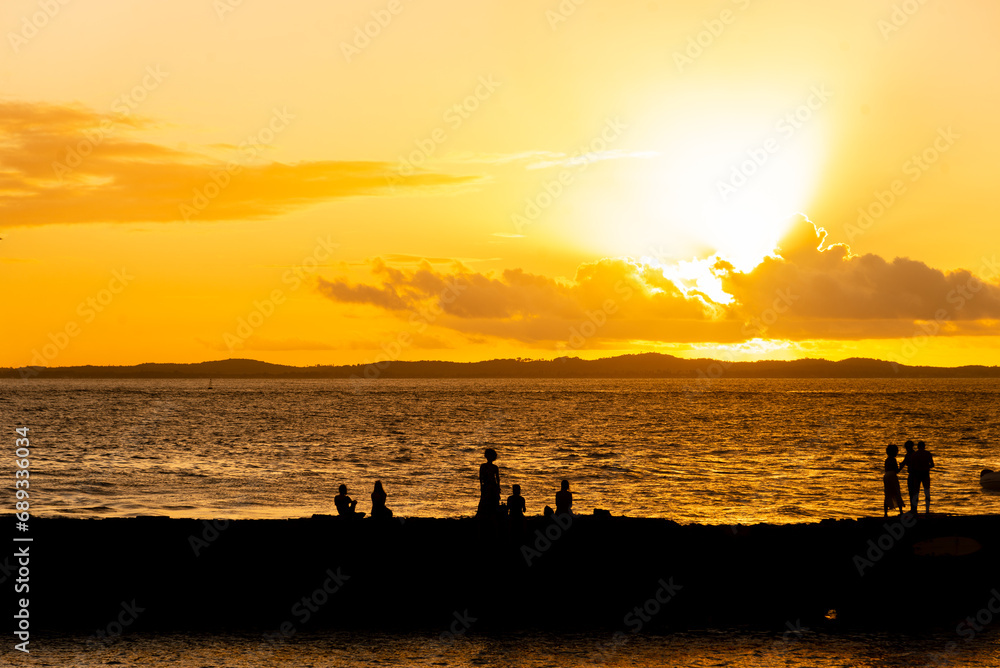 Silhouette of tourists at dramatic orange sunset against the beach.