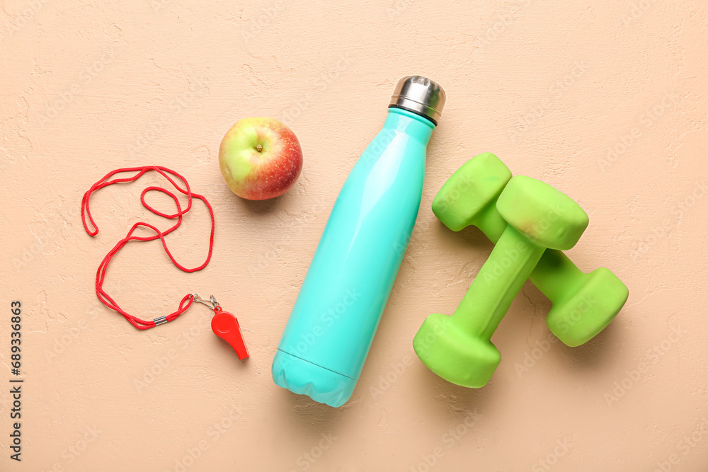 Naklejka premium Dumbbells, apple, skipping rope and bottle for water on beige background