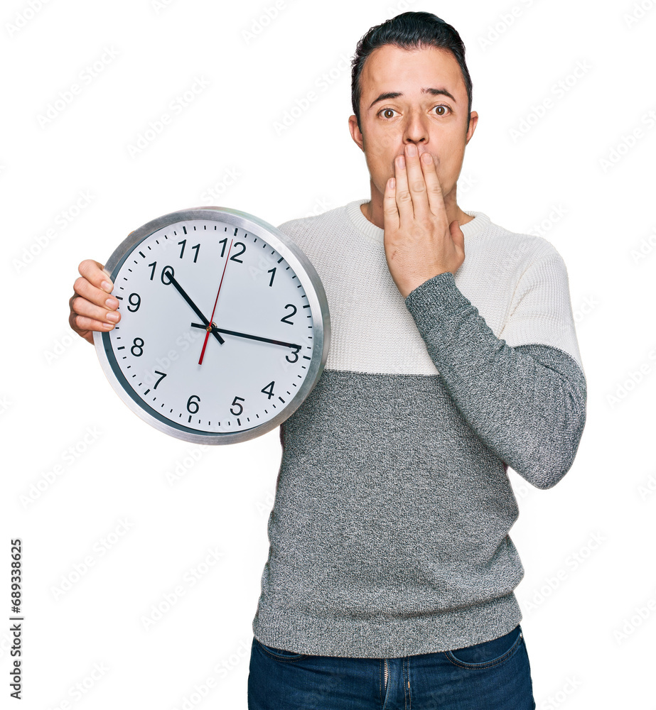 Handsome young man holding big clock covering mouth with hand, shocked and afraid for mistake. surprised expression Handsome young man holding big clock covering mouth with hand, shocked and afraid for mistake. surprised expression