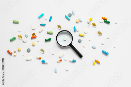 Fish oil capsules with different pills and magnifying glass on white background