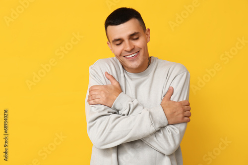 Handsome young man hugging himself on yellow background