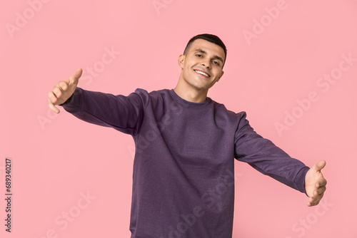 Handsome young man opening arms for hug on pink background