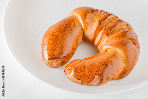Tasty fresh crescent roll with golden crust, on light plate, selective focus.