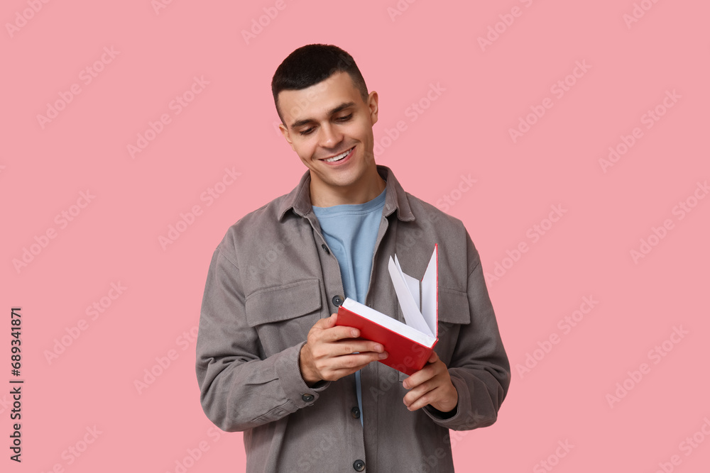 Handsome young man reading book on pink background Handsome young man reading book on pink background