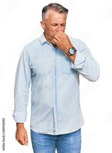 Middle age grey-haired man wearing casual clothes smelling something stinky and disgusting, intolerable smell, holding breath with fingers on nose. bad smell © Krakenimages.com