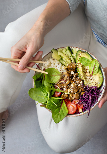 A woman in light clothes holds a bowl of salad and chopsticks in her hands. The concept of proper nutrition. Salad of mushrooms, rice, avocado and vegetables.