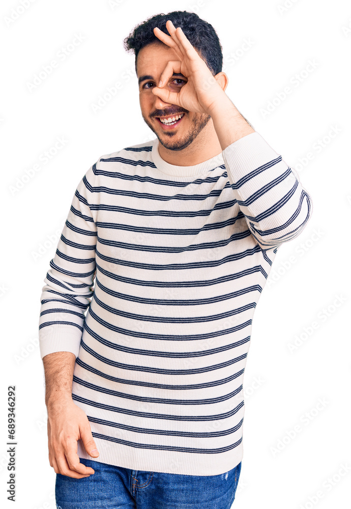 Young hispanic man wearing casual clothes doing ok gesture with hand smiling, eye looking through fingers with happy face. Young hispanic man wearing casual clothes doing ok gesture with hand smiling, eye looking through fingers with happy face.