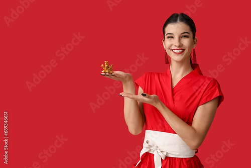 Beautiful young happy woman pointing at golden dragon figurine on red background. Chinese New Year celebration