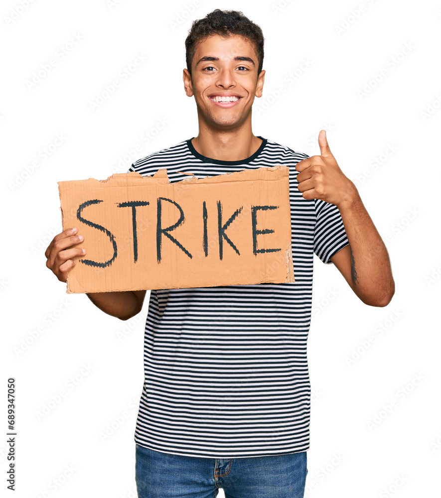 Young handsome african american man holding strike banner cardboard smiling happy and positive, thumb up doing excellent and approval sign Young handsome african american man holding strike banner cardboard smiling happy and positive, thumb up doing excellent and approval sign