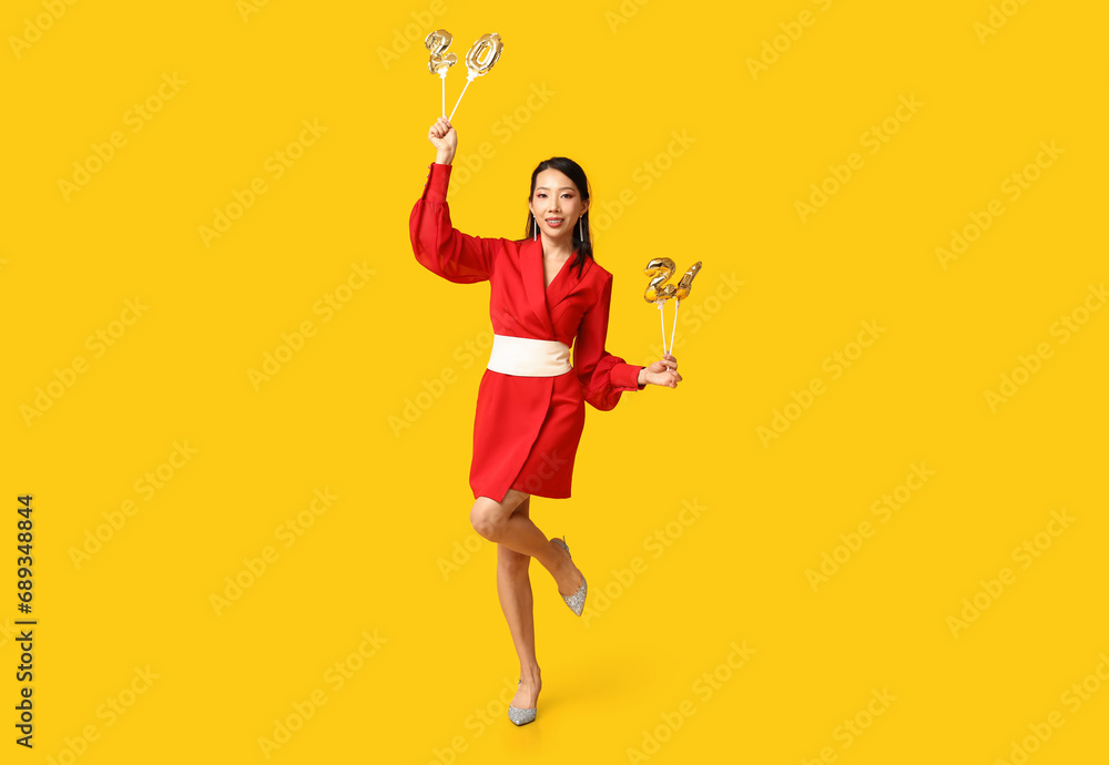 Beautiful young happy Asian woman with figure 2024 made of balloons on yellow background. Chinese New Year celebration