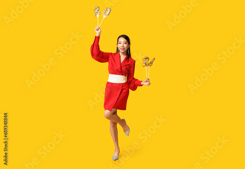 Beautiful young happy Asian woman with figure 2024 made of balloons on yellow background. Chinese New Year celebration © Pixel-Shot