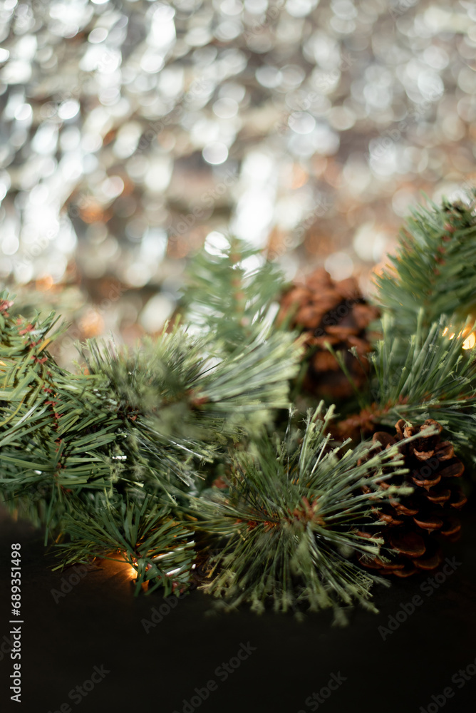 Close-up of a green branch of a Christmas tree with a garland shines against the background of crumpled foil. Decorated with a pine cone. Place for text. Postcard. Merry Christmas and Happy New Year Close-up of a green branch of a Christmas tree with a garland shines against the background of crumpled foil. Decorated with a pine cone. Place for text. Postcard. Merry Christmas and Happy New Year