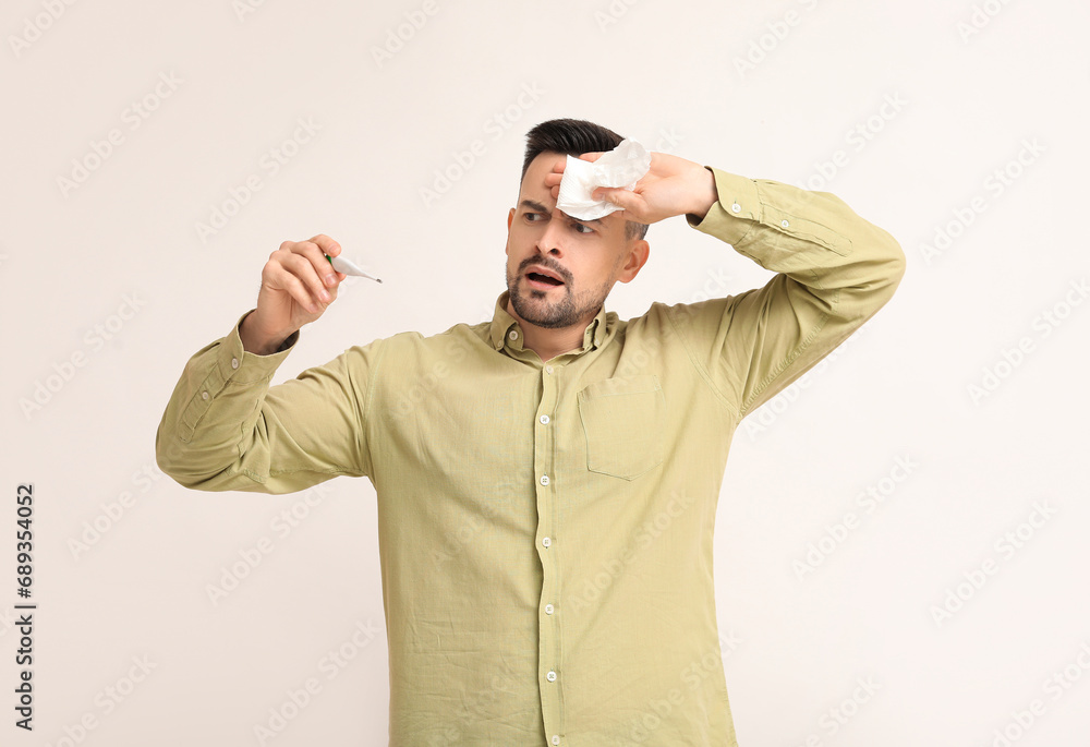 Sick young man with tissue and thermometer on light background Sick young man with tissue and thermometer on light background