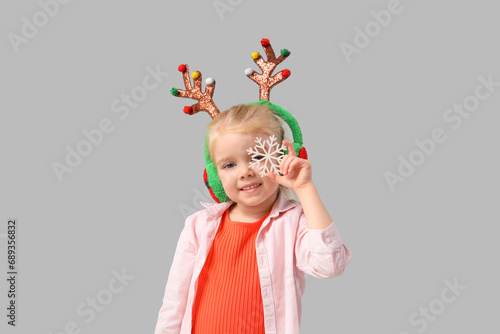 Cute little girl in reindeer horns with snowflake on light background