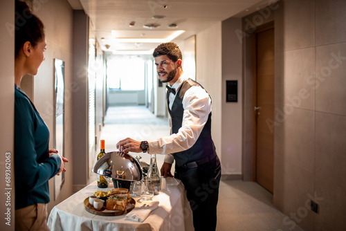 Male room service hotel staff waiter serving tray to hotel guest photo
