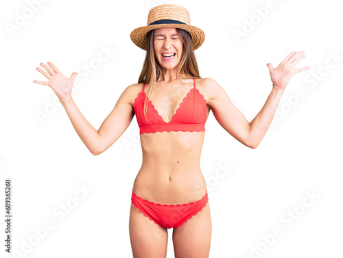 Beautiful brunette young woman wearing bikini celebrating mad and crazy for success with arms raised and closed eyes screaming excited. winner concept