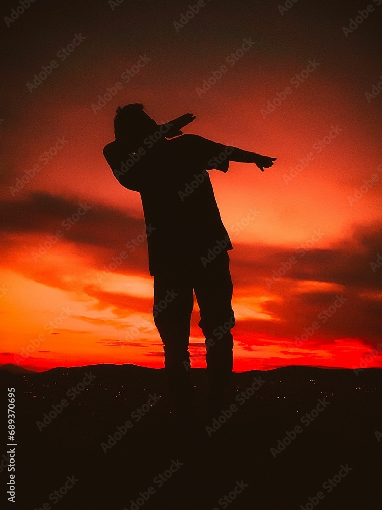 silhouette of person holding something against sunset sky with black ground