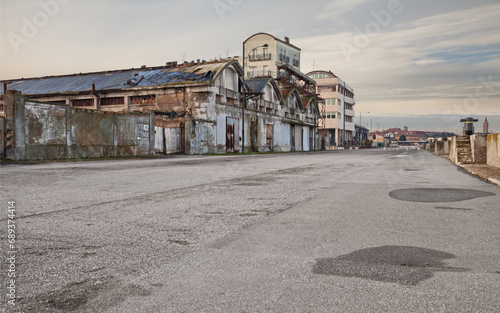 wide street in the suburbs of the city with abandoned warehouse and factory - desolate landscape in the outskirts of the town with empty road and ruined factories © ermess