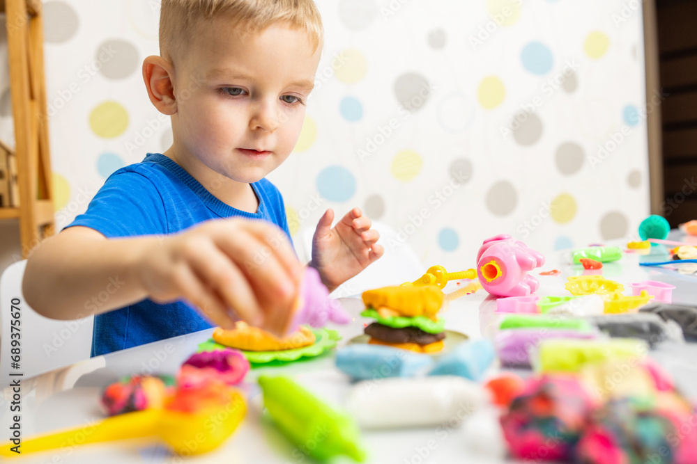 Little boy enthusiastically plays with plasticine, play dough on white table Little boy enthusiastically plays with plasticine, play dough on white table