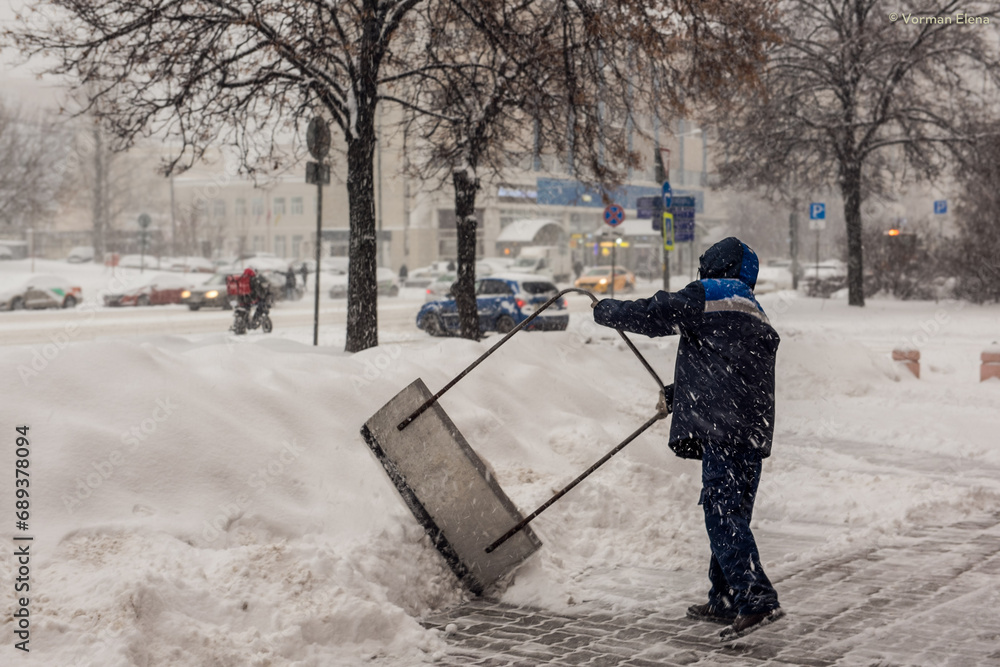 A labouring man shoveling away snow in Moscow, struggling with big banks of snow A labouring man shoveling away snow in Moscow, struggling with big banks of snow