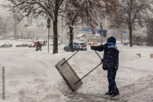 Fototapeta A labouring man shoveling away snow in Moscow, struggling with big banks of snow
