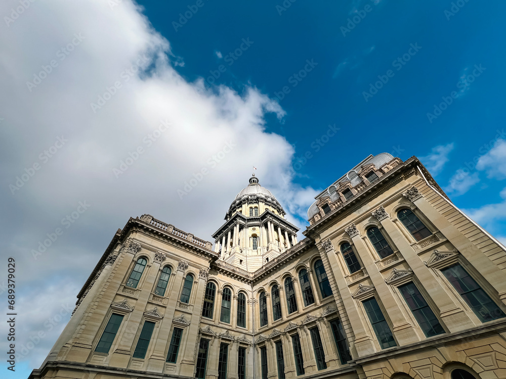 Rear views of the Illinois State Capitol Building in Springfield, Illinois, USA. Cloudy blue skies overhead. Sunlight shines down upon the dome of the building.
