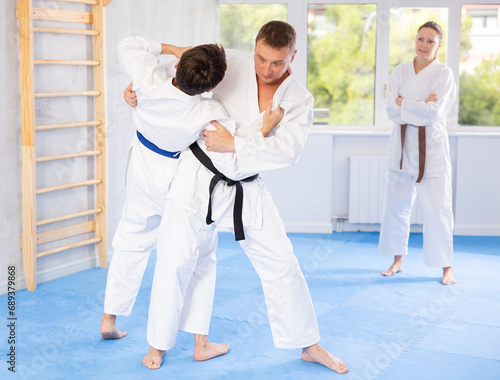 Two men during classes, training improve and practice wrestling with opponent in technique of martial arts. Third woman partner performs warm-up before lesson