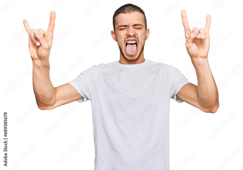 Hispanic young man wearing casual white t shirt shouting with crazy expression doing rock symbol with hands up. music star. heavy concept. Hispanic young man wearing casual white t shirt shouting with crazy expression doing rock symbol with hands up. music star. heavy concept.