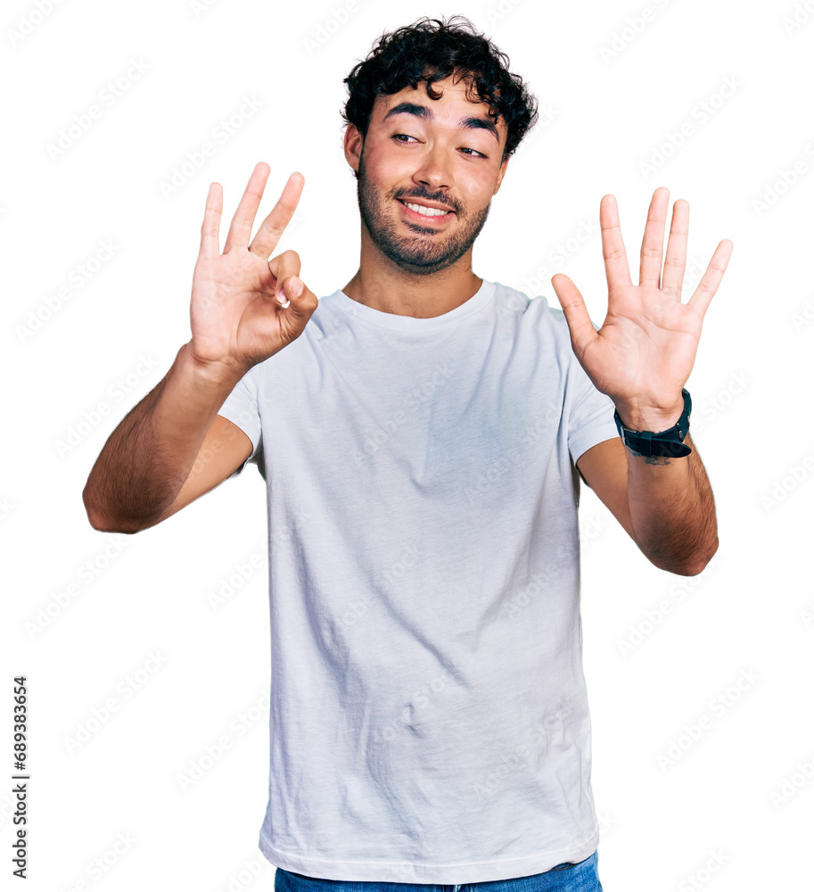 Fototapeta premium Hispanic young man with beard wearing casual white t shirt showing and pointing up with fingers number eight while smiling confident and happy.